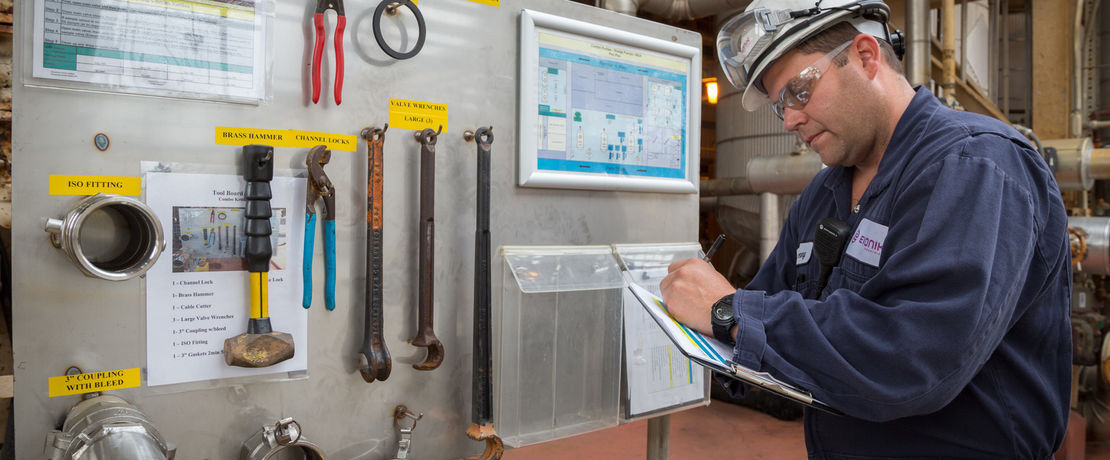 man working in a production facility writing on a clipboard